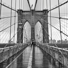 People Walking On Wet Brooklyn Bridge Against Sky
