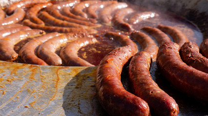 Tasty Sausages on Commercial Griddle Hotplate.Smoke Rises above Frying Sausages. Street Food Market...