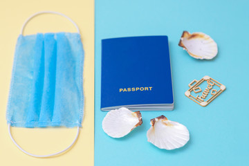 Travel concept during coronavirus. Travel concept with a passport, medical mask and seashells on a blue and yellow background. Selective focus.