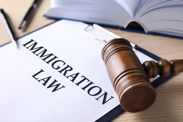 Clipboard with words IMMIGRATION LAW and gavel on wooden table, closeup