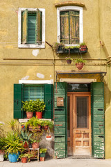 Colorful house facade with wooden shutters on windows and door and potted plants on windowsill