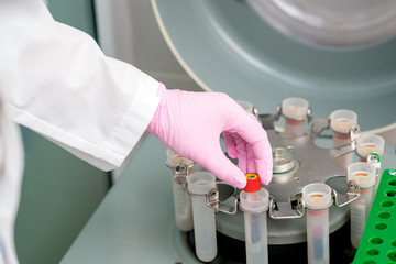 Male hand is puting test tube to centrifuge machine wearing protective gloves.