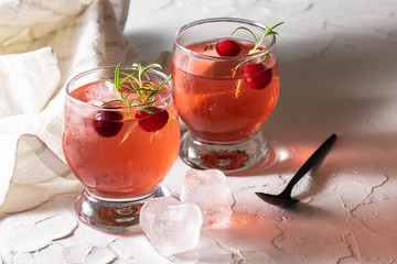 Fresh cold cranberry drink with ice and rosemary on white rustic background. Summer refreshing drink close up.