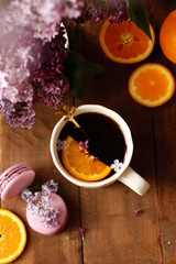 A cup of healthy black tea with a slice of orange on a darnvy dark table with a bouquet of lilac lilac and a cupcake, flat lay. Space for text