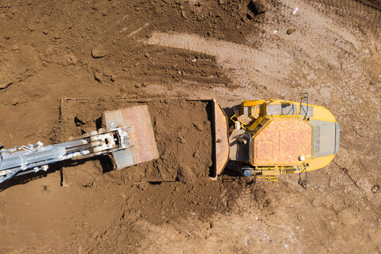 Excavator Loading Soil Onto An Articulated Hauler Truck, Top Down Aerial View.
