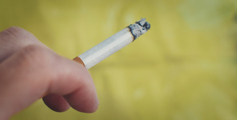hand holding a cigarette with yellow-green background