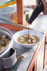 street food vendor of bakso or meatball. man pour some sweet soy sauce