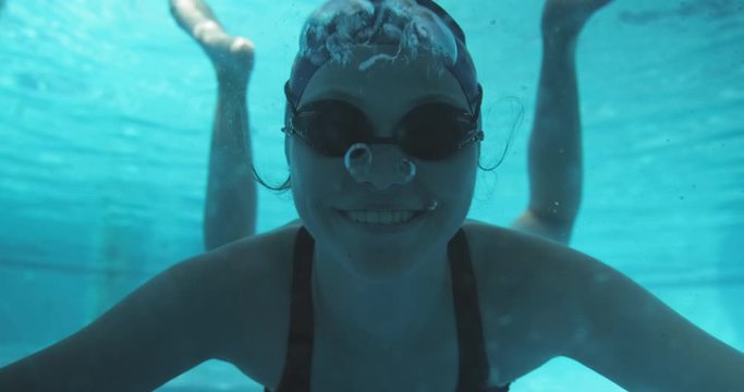 Athletic teenager girl swimmer underwater in blue outdoor pool, looking at camera