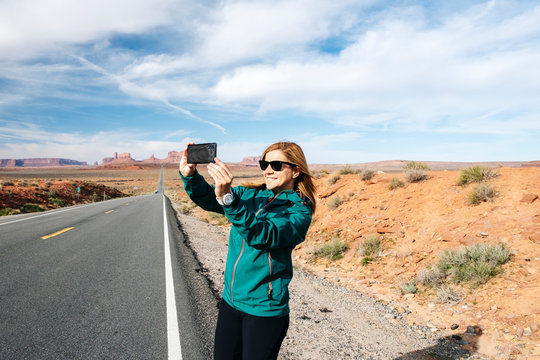 A woman tours taking selfie photo with phone at the famous Monument Valley desert highway in Utah, USA.