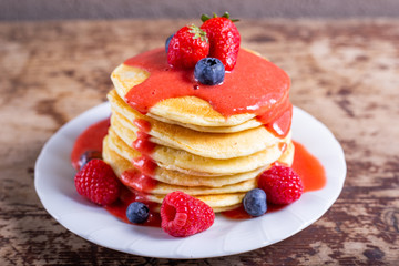 Stack of homemade pancakes with syrup and berries. Typical American breakfast or snack.