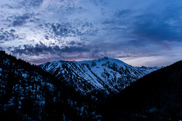 A picturesque landscape view of the snow capped Pyrenees mountain range and the dramatic cloudy sky in the Vall de Sorteny (Andorra) natural park on a cold winter evening during sunset