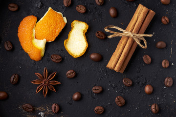 Roasted whole coffee beans, tied sticks of cinnamon, anise and orange zest on a dark background