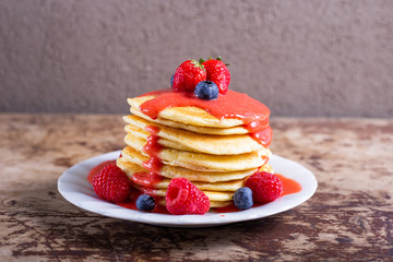 Stack of homemade pancakes with syrup and berries. Typical American breakfast or snack.