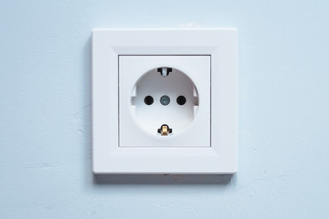 White socket with grounding contacts on a blue wall background. Electricity consumption concept.