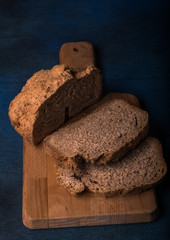 A delicious freshly made bread cut into slices on a wooden board. Blue background. Vertical format.