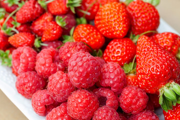 Ripe raspberries, strawberries and wild strawberries on a plate