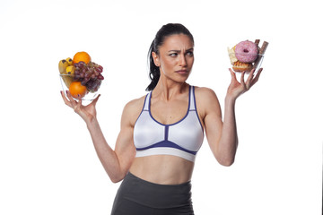 Sexy brunette woman in fitness suit eating fruits and candies