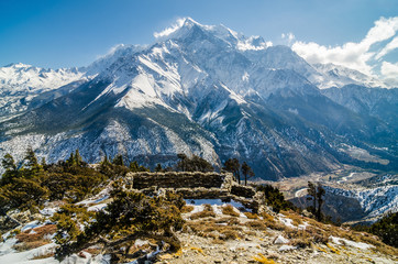 Ruined house on the rocky mountain slope against Mt. Nilgiri in sunny winter day. Yak kharka, a pasture above Marpha village, Annapurna circuit / Jomson trek, Nepal.