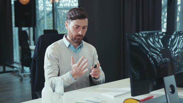 Attractive man disinfects hands with antiseptic before working on laptop workplace quarantine computer hygiene business office worker epidemic hygienic disinfection pandemic keyboard slow motion