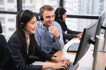 Happy smiling asian woman call center and operator with colleague wearing headsets working on...