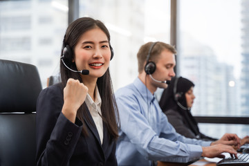 Happy smiling asian woman call center and operator wearing headsets working on computer and talking...