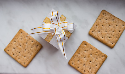 Flat lay. Top view. New Year's gift with bow of gold ribbons and lean ruddy crackers with bran on white background