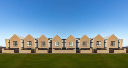 Front view of a symmetrical row of modern two storey townhouses along a footpath and lawn against a blue sky background in an Australian suburb with lots of copy space 