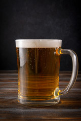 glass of barley beer with foam on a dark wooden background, alcoholic beverage