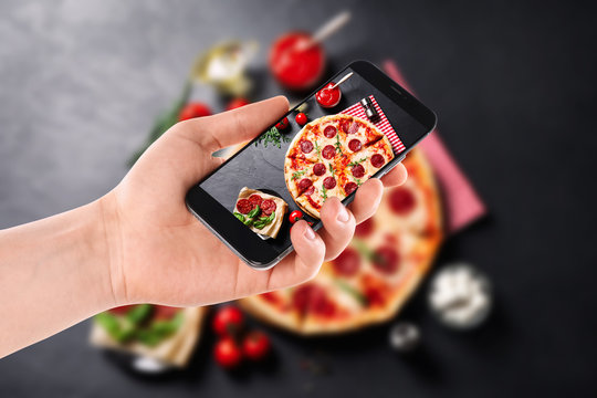 Blogger taking picture of delicious pepperoni pizza at table, closeup. Food photography