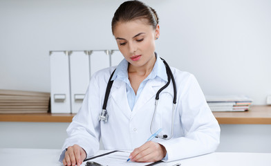 Woman-doctor sitting and working at clinic office. Portrait of female physician. Medicine concept