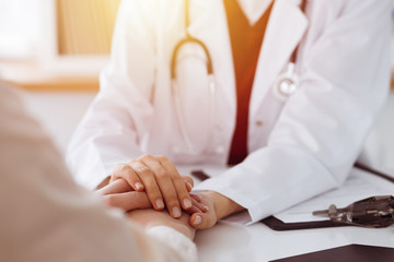 Hands of unknown woman-doctor reassuring her female patient in sunny room, close-up