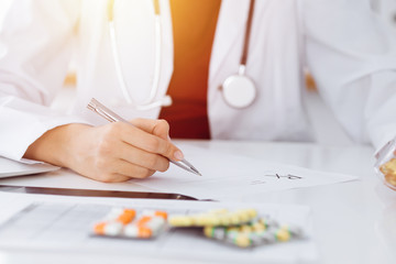 Unknown woman-doctor fills up prescription form in sunny room, close-up