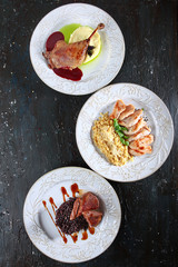 Three different dishes in one photo. Turkey with chili sauce. Duck leg with cherry sauce. Roast duck with brown rice. Photo on a dark textured background. Copy of the space. Page for the menu.