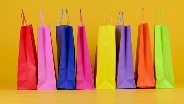 Funny little dog breed Jack Russell Terrier goes on the background of shopping bags on a yellow studio bashound. Shopping concept