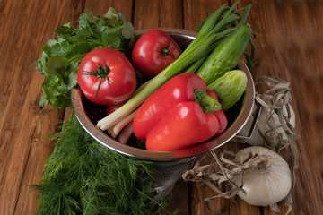 Fresh red tomatoes, bell pepper, cucumbers, onions and fresh herbs on a wooden background
