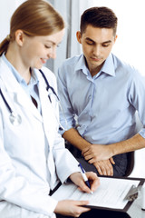 Female doctor holding application form while consulting man patient in hospital office. Medicine and healthcare concept