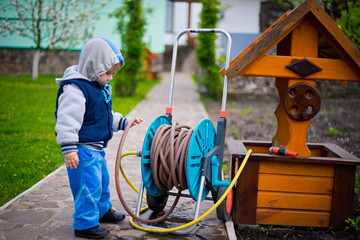 Cute caucasian toddler kid child boy playing with a garden watering hose 