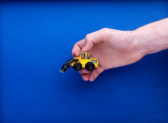 Maquette miniature tracto pelle engin de chantier saisie par une main pour illustration chantier, construction protection, jeu sur fond bleu
