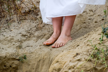 Legs of a girl in a white dress on edge of a cliff. The sand is falling from the edge of the cliff.