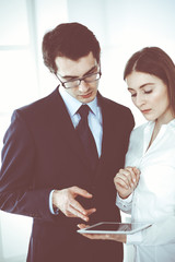 Obraz premium Businessmen and woman using tablet computer in modern office. Colleagues or company managers at workplace. Partners discussing contract. Business concept