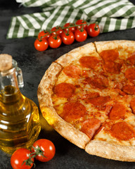 Pepperoni pizza on a black background with tomato butter and garlic in composition