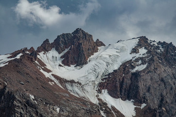 rocky mountain peak with snow and glacier in cloudy weather with clouds