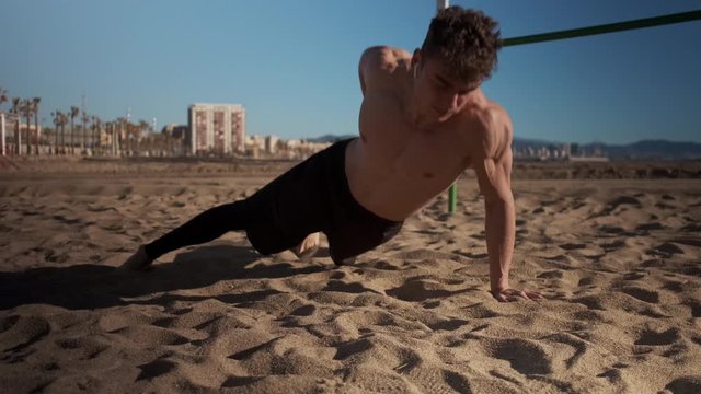 Young strong muscular man doing hard exercises during functional training on city beach