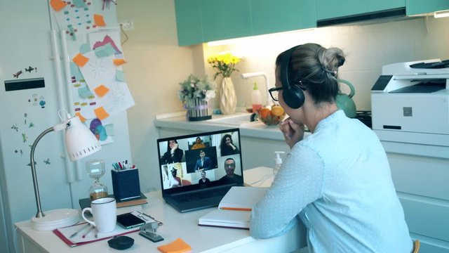 A worker in headset talks to people via laptop while staying home during pandemic. Zoom, videocall , video conference, online meeting, working remotely concept.