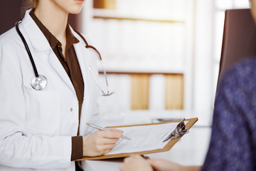Doctor and patient discussing current health examination while sitting in sunny clinic. Perfect...