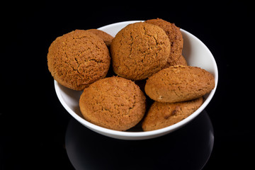 Appetizing oatmeal cookies in a white plate close-up on a black mirror background. Horizontal orientation. 