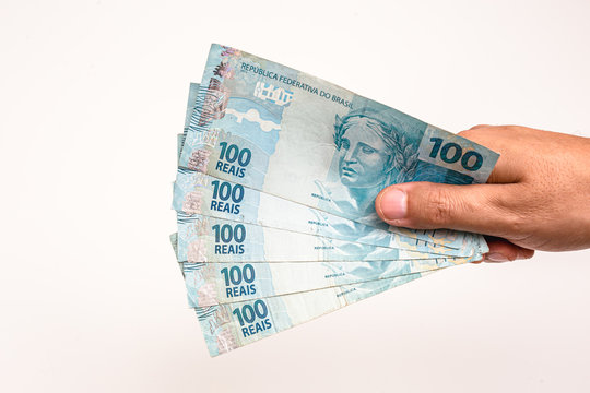 100 reais bills from Brazil, held by male hand on isolated white background. Banknotes of one hundred reais from brazil, payday.