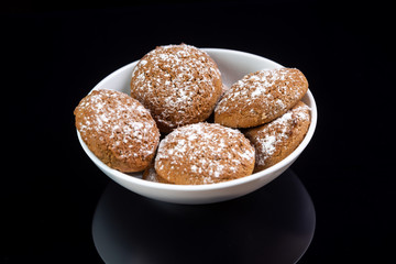 Appetizing oatmeal cookies sprinkled with icing sugar in a white plate close-up on a black mirror background. Horizontal orientation. 