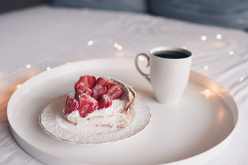 Homemade unbaked strawberry cake with cp of tea on white tray in bed closeup. Good morning. Breakfast time. Birthday surprise.