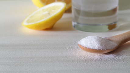 powdered Vitamin C on wooden spoon with glass of water and cut lemon on white background